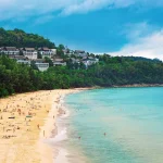 A crowded beach with white sand and clear blue water.