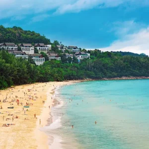 A crowded beach with white sand and clear blue water.