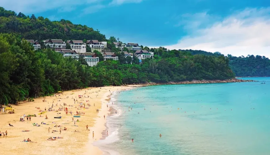 A crowded beach with white sand and clear blue water.