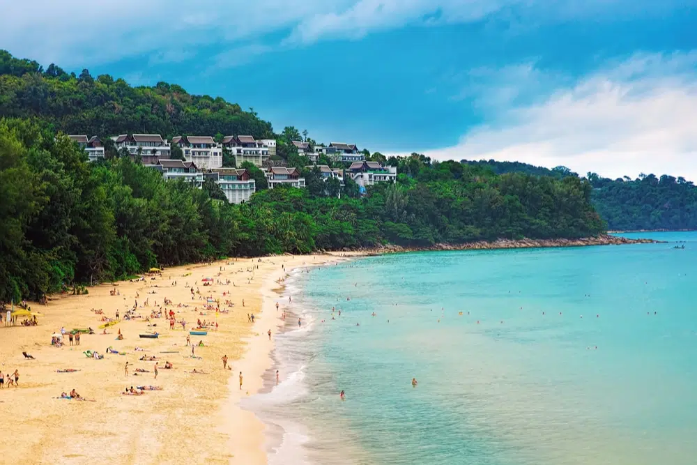 A crowded beach with white sand and clear blue water.