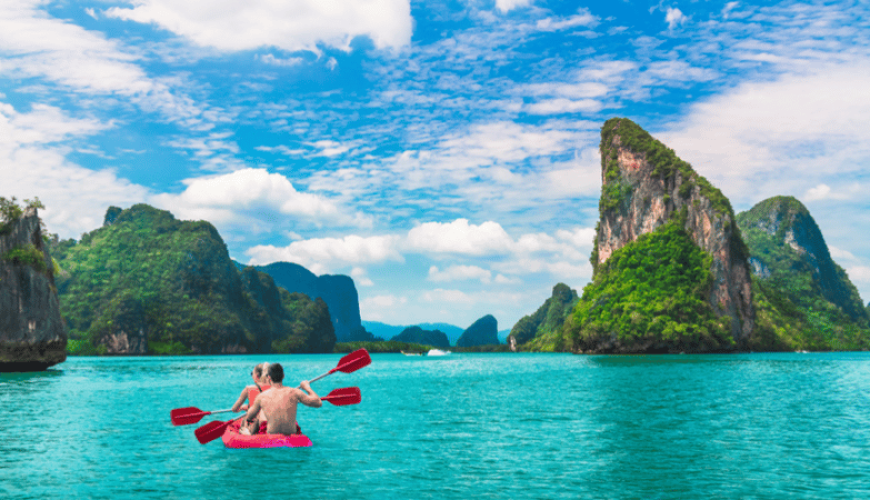 A couple kayaking in Ko Tapu, surrounded by towering limestone cliffs and clear waters.