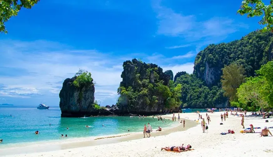 Sunny day at Krabi Island beach, people sunbathing and boats anchored offshore