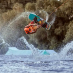 Person performing an aerial trick on a wakeboard with a splash of water in the background.