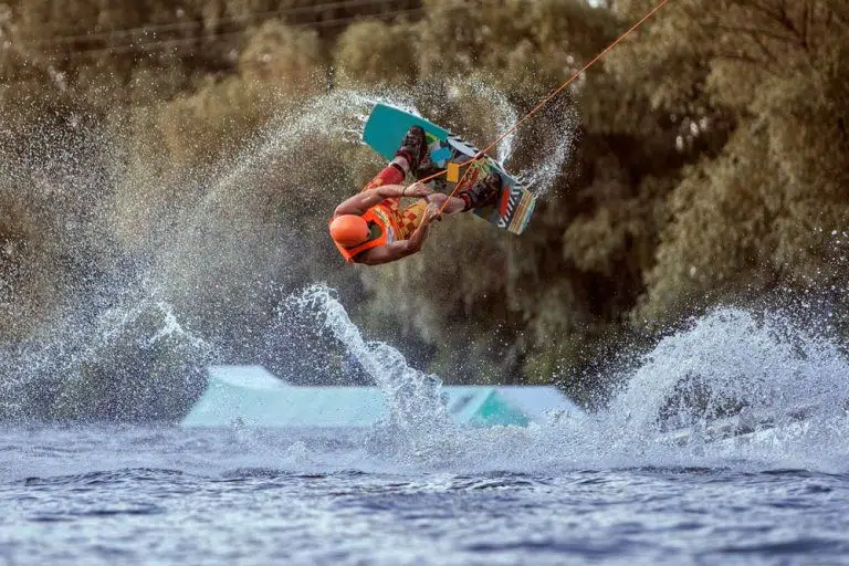 Person performing an aerial trick on a wakeboard with a splash of water in the background.
